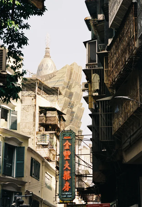 A narrow street framed by older buildings, with a pharmacy sign and a tall gold-colored building beyond.