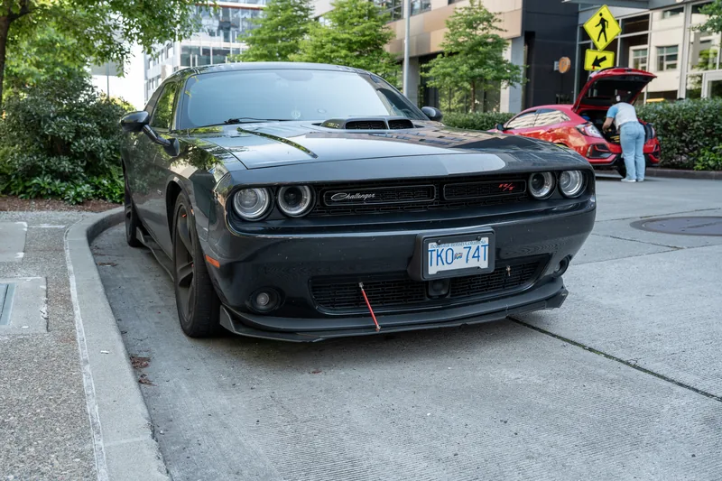 A black car parked beside a leafy street.