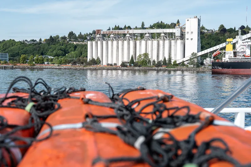 Orange life jackets aboard a boat near a cargo terminal.