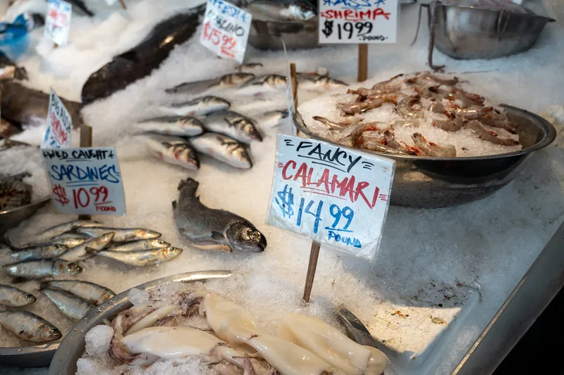 Seafood displayed on ice with handwritten price signs.
