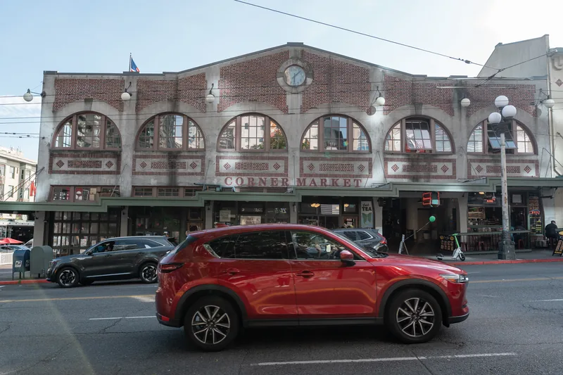 A red car parked outside a brick market building.