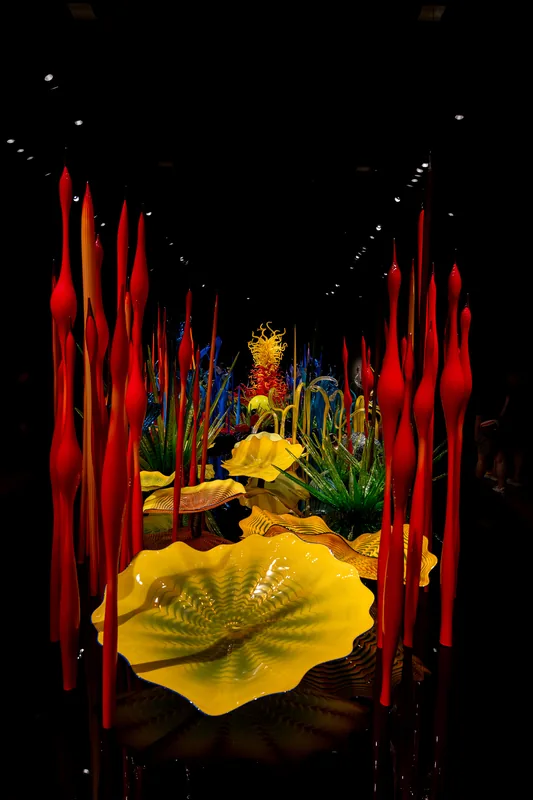 An illuminated yellow glass sculpture in a dark gallery.