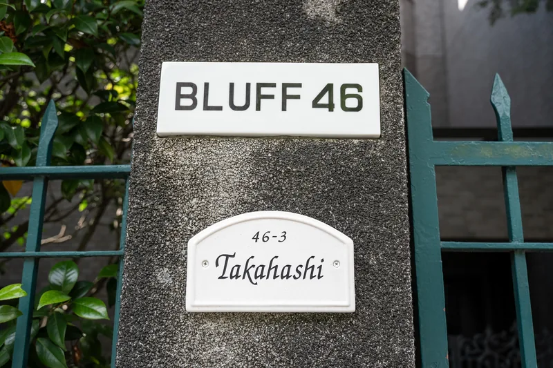 A small sign attached to a leafy garden fence.