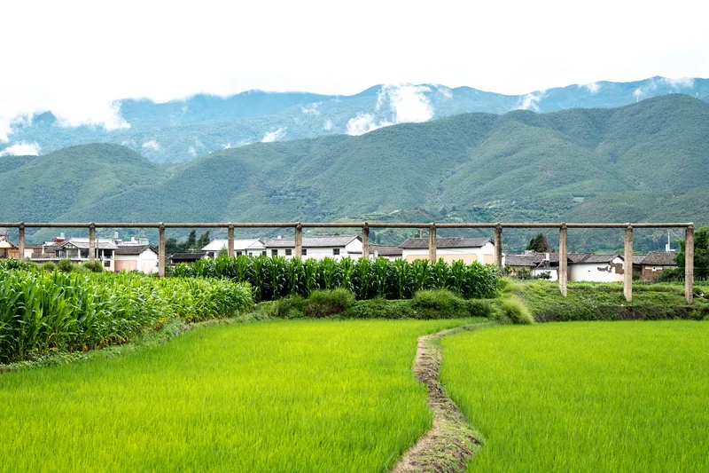 Green fields and a village beneath cloudy mountains.